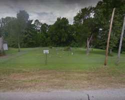 The burial site bounded by a chain-link fencing net from three sides, the west side bounded by lined trees.